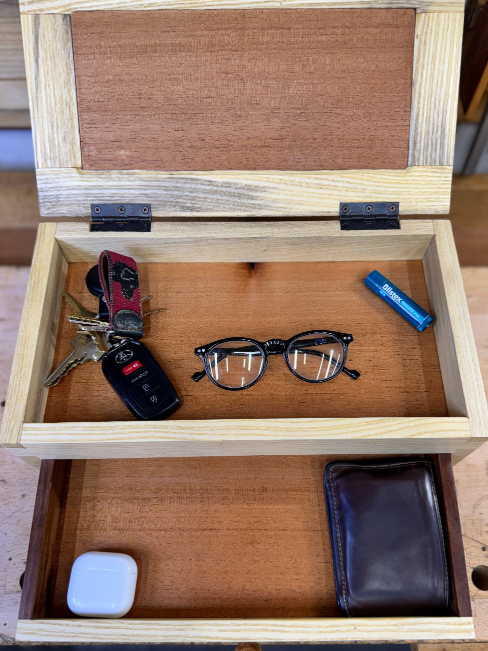 Wooden box with keys, glasses, and other items on a wooden surface